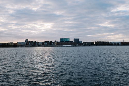 Free City skyline at dawn overlooking a calm river with soft clouds above. Stock Photo
