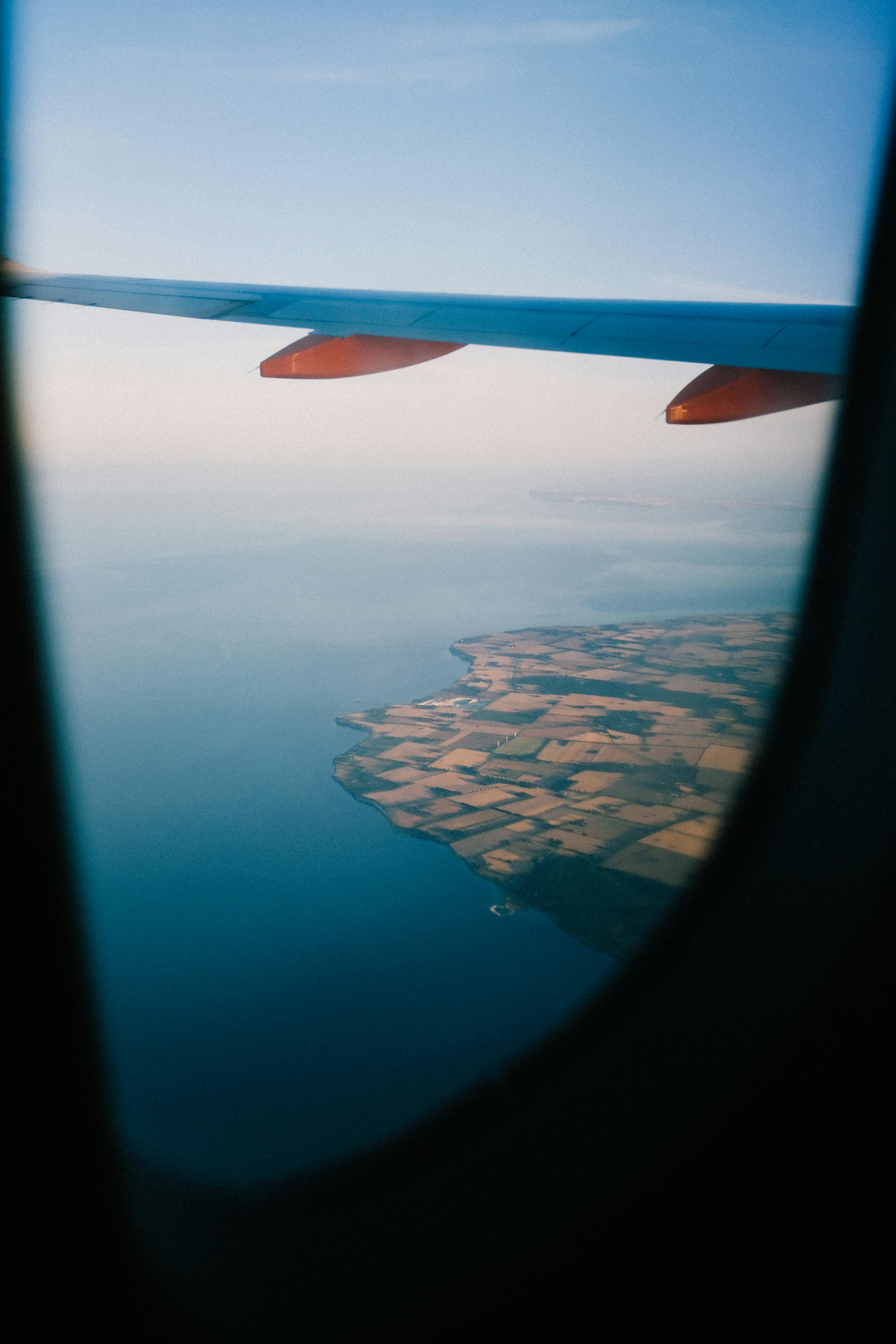 Scenic view of coastline and fields from an airplane window, capturing the beauty of travel.