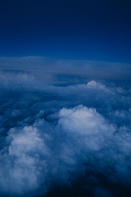 Free Dramatic aerial view of fluffy clouds and an overcast sky with a deep blue hue. Stock Photo
