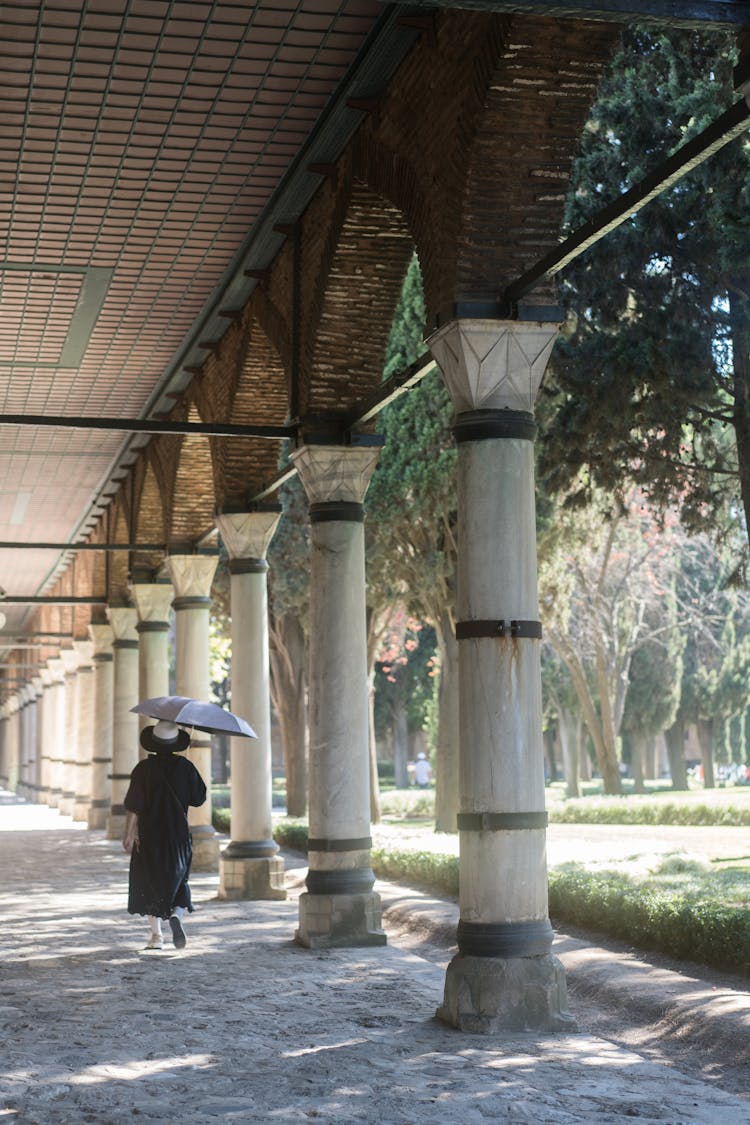 Woman Walking With Umbrella Under An Old Architecture With Arches