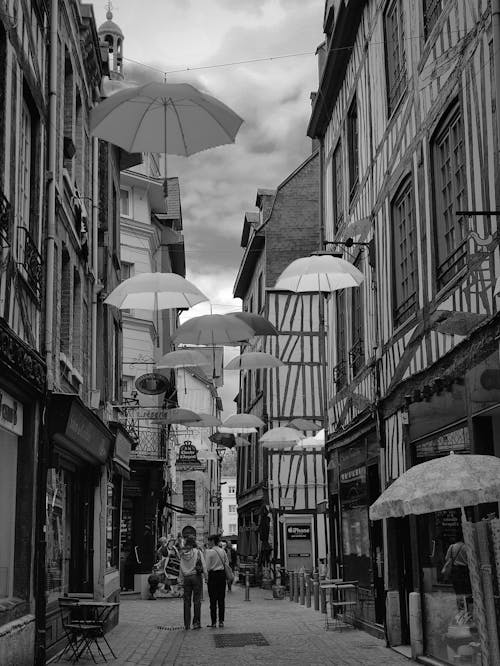 A Grayscale Photo of People Walking on the Street With Hanging Umbrellas