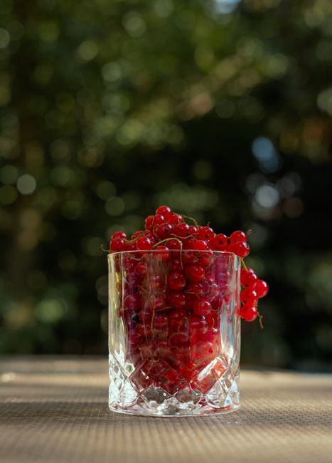 A vertical shot of fresh redcurrants in a glass with a blurred outdoor background.