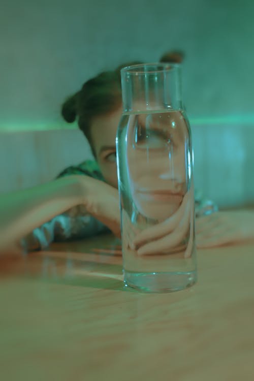 Distorted Face of a Woman Behind a Glass Bottle 
