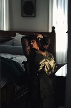 A woman in nightwear stretches comfortably in a softly lit bedroom.