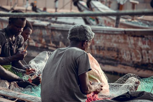 Free Group of men fixing fishing nets on rustic boats in a bustling harbor. Stock Photo