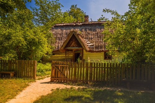 Free Charming rural house with a traditional thatched roof surrounded by lush greenery and a wooden fence. Stock Photo