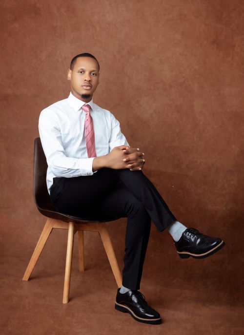 Free Portrait of a man in business attire seated in studio against brown backdrop. Stock Photo