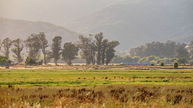 A tranquil view of a train passing through a field with mountains.