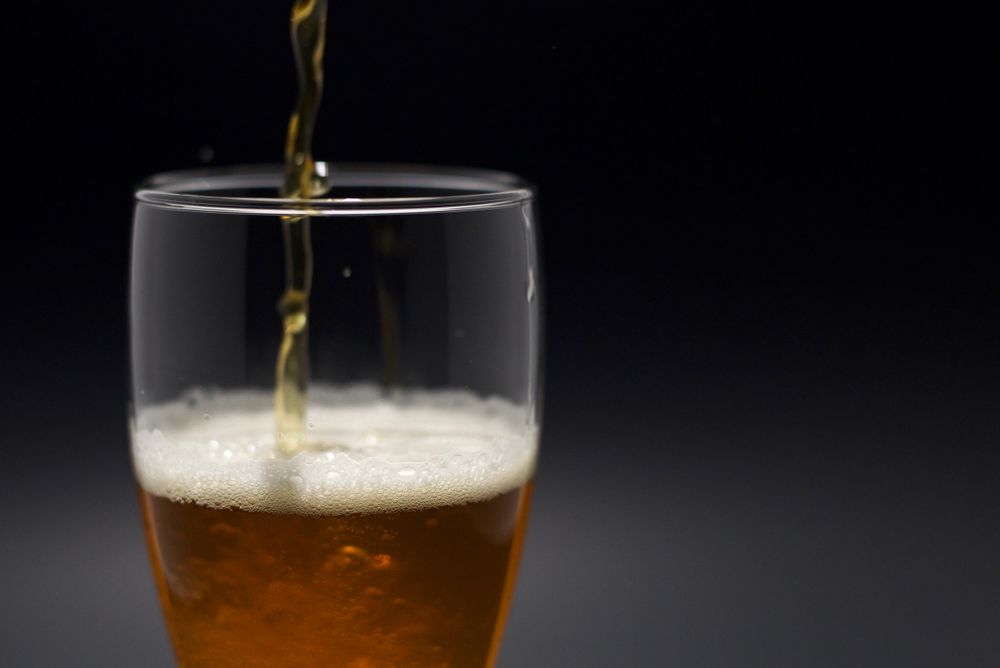 Birra versata in un bicchiere su sfondo scuro, immagine stock