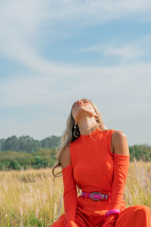 Free A stylish woman in an orange dress poses outdoors, capturing vibrant fashion in a serene field setting. Stock Photo