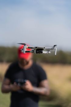 A sleek drone flying in focus outdoors as the blurred operator controls it.