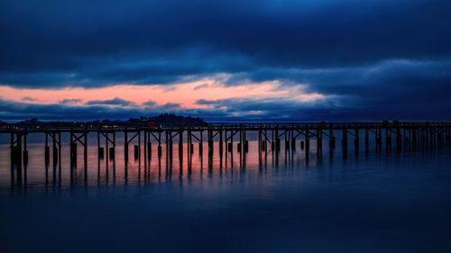 Free A tranquil wooden pier silhouetted against a vibrant twilight sky over calm ocean waters. Stock Photo