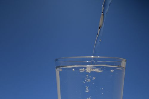 Free A close-up of water gently pouring into a clear glass against a blue background. Stock Photo