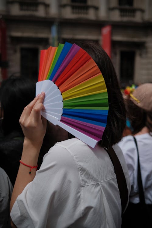 Person in White Blouse Holding a Rainbow Hand Fan 