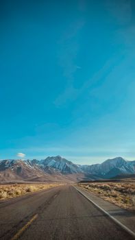 Long empty road leading to majestic snow-capped mountains at Mammoth Lakes, California under a clear blue sky.