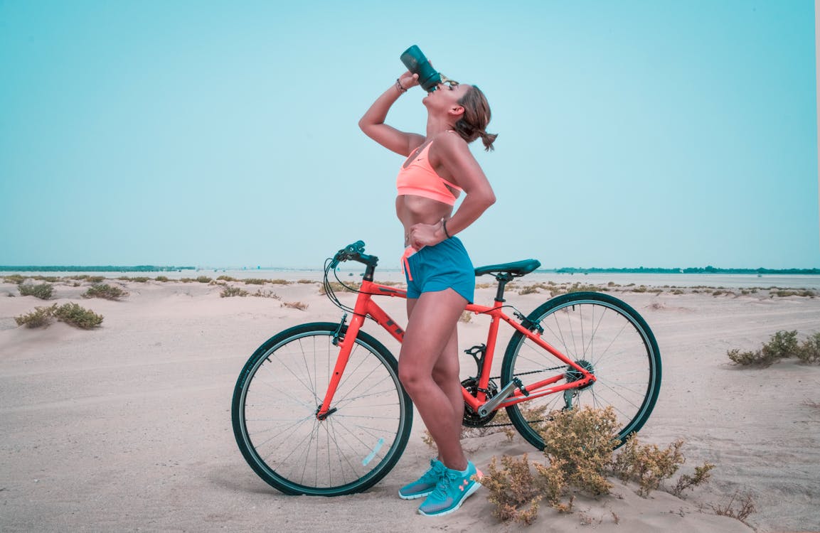 Woman drinks from the bike water bottle that she just took from the bike water bottle cage