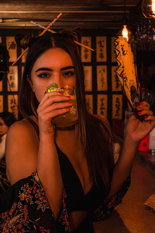 Free Woman in a stylish bar sipping cocktail with exotic decor holding a fan, creating a festive mood. Stock Photo
