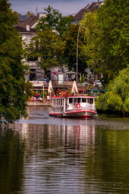 Free A white riverboat cruising peacefully down a scenic city canal surrounded by lush greenery. Stock Photo