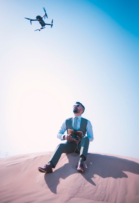 Businessman in suit flying drone over Dubai desert. Clear sunny sky, modern technology in mesmerizing landscape.