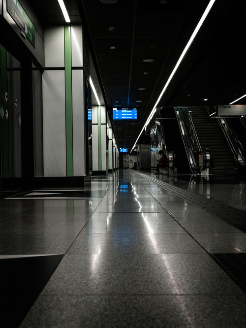 Free Dimly lit modern subway station featuring escalators, glossy floors, and information signs. Stock Photo