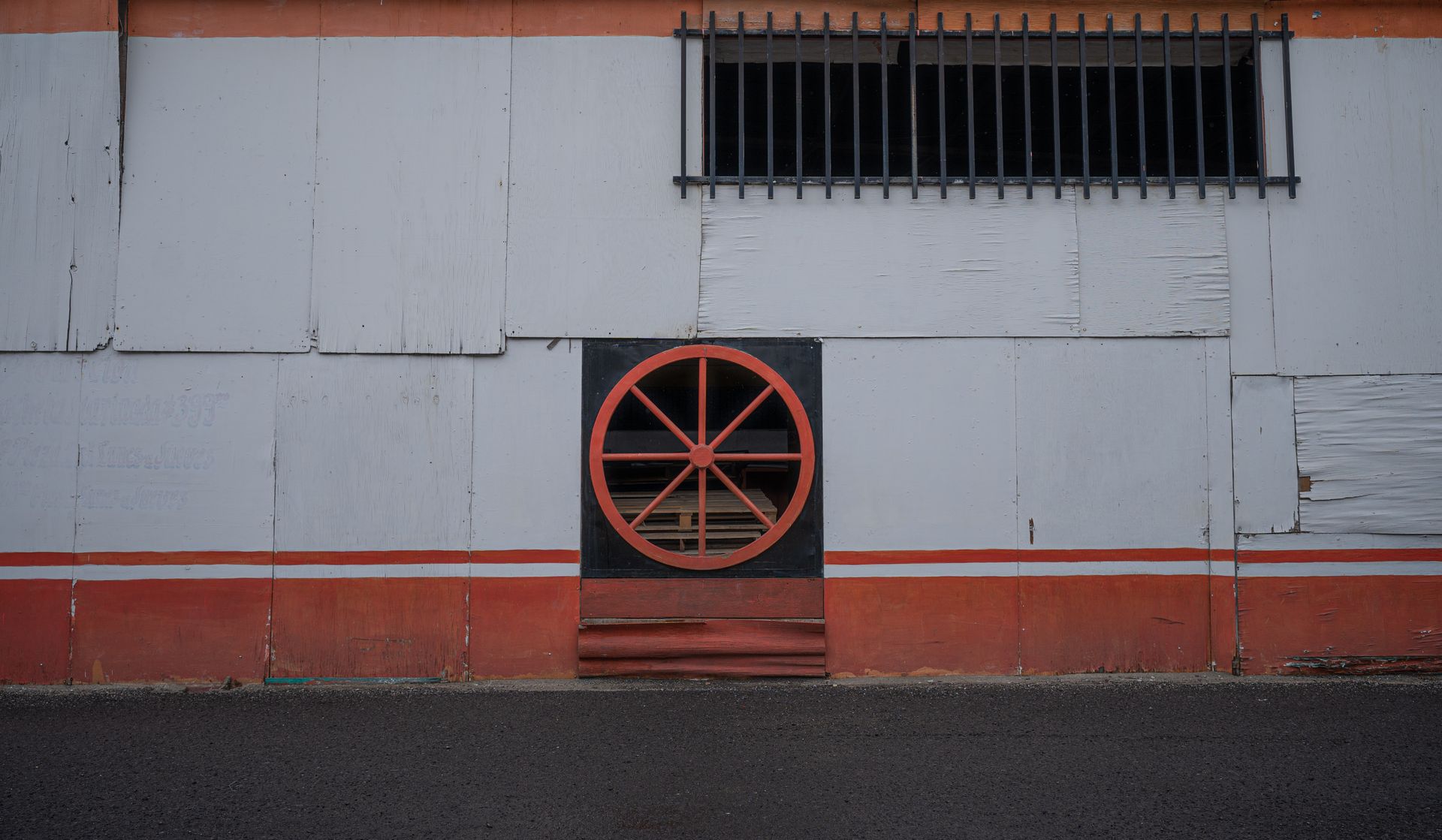 A close-up view of an industrial wall featuring a circular ventilation wheel and barred window.