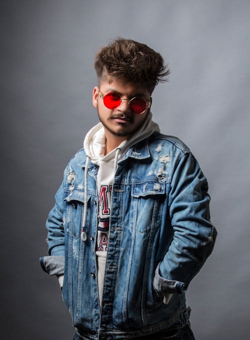 Man in Denim Jacket Wearing Red Sunglasses on Grey Background