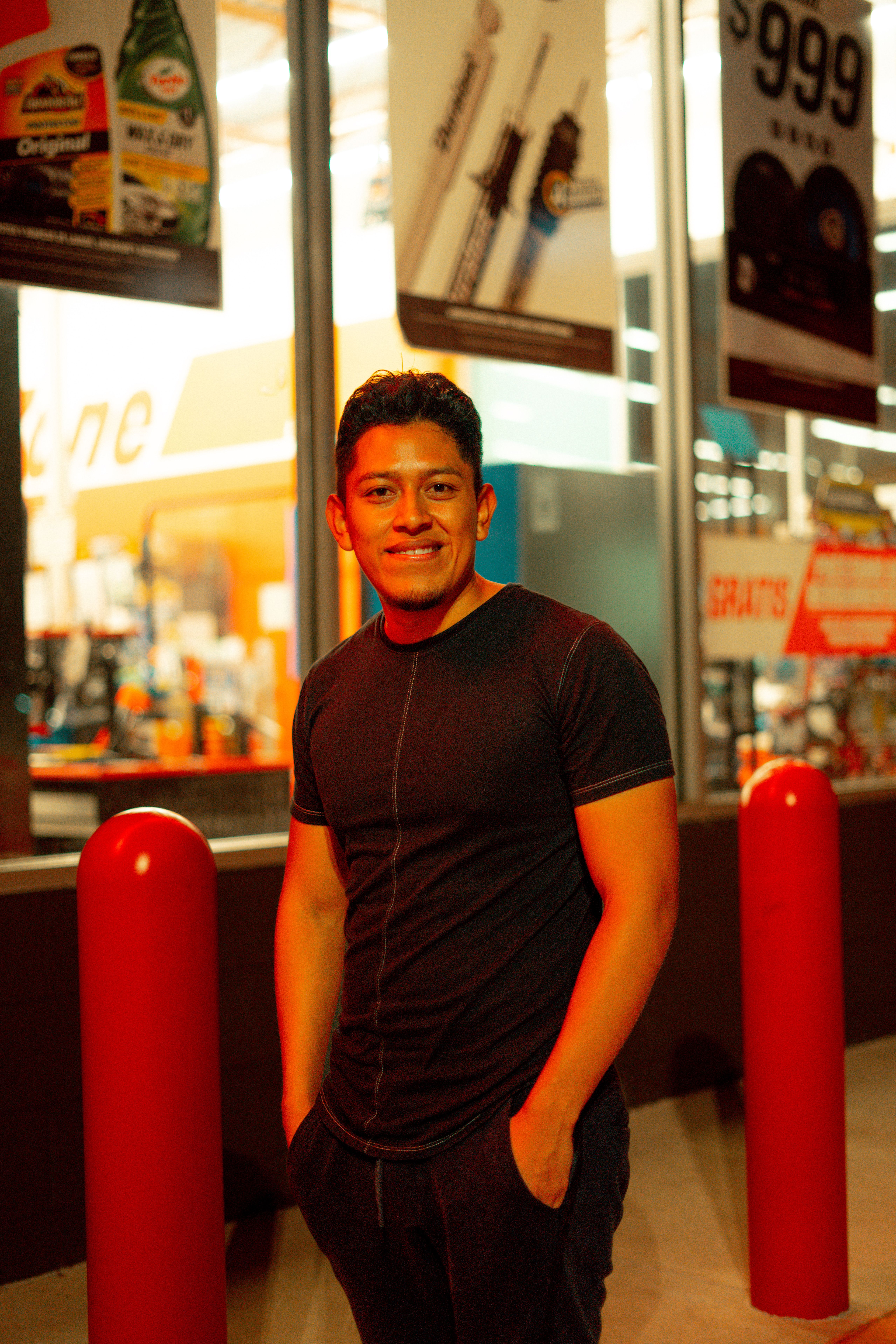 A smiling man stands confidently on a city night street with colorful lights.