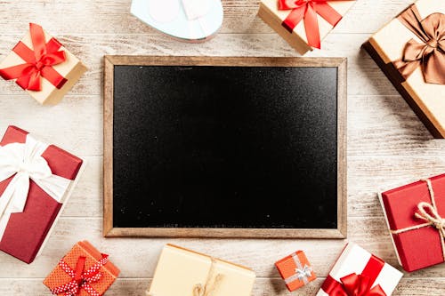 빨간 선물 상자로 둘러싸인 갈색 나무 프레임 칠판