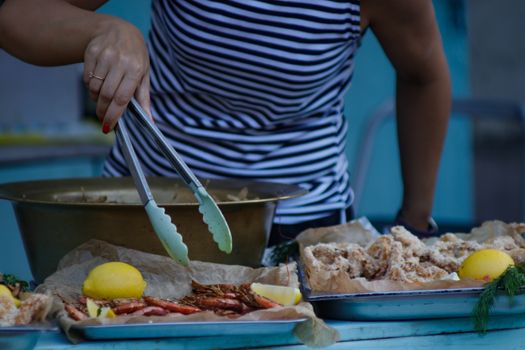 Person in striped shirt preparing fried seafood with lemons using tongs.