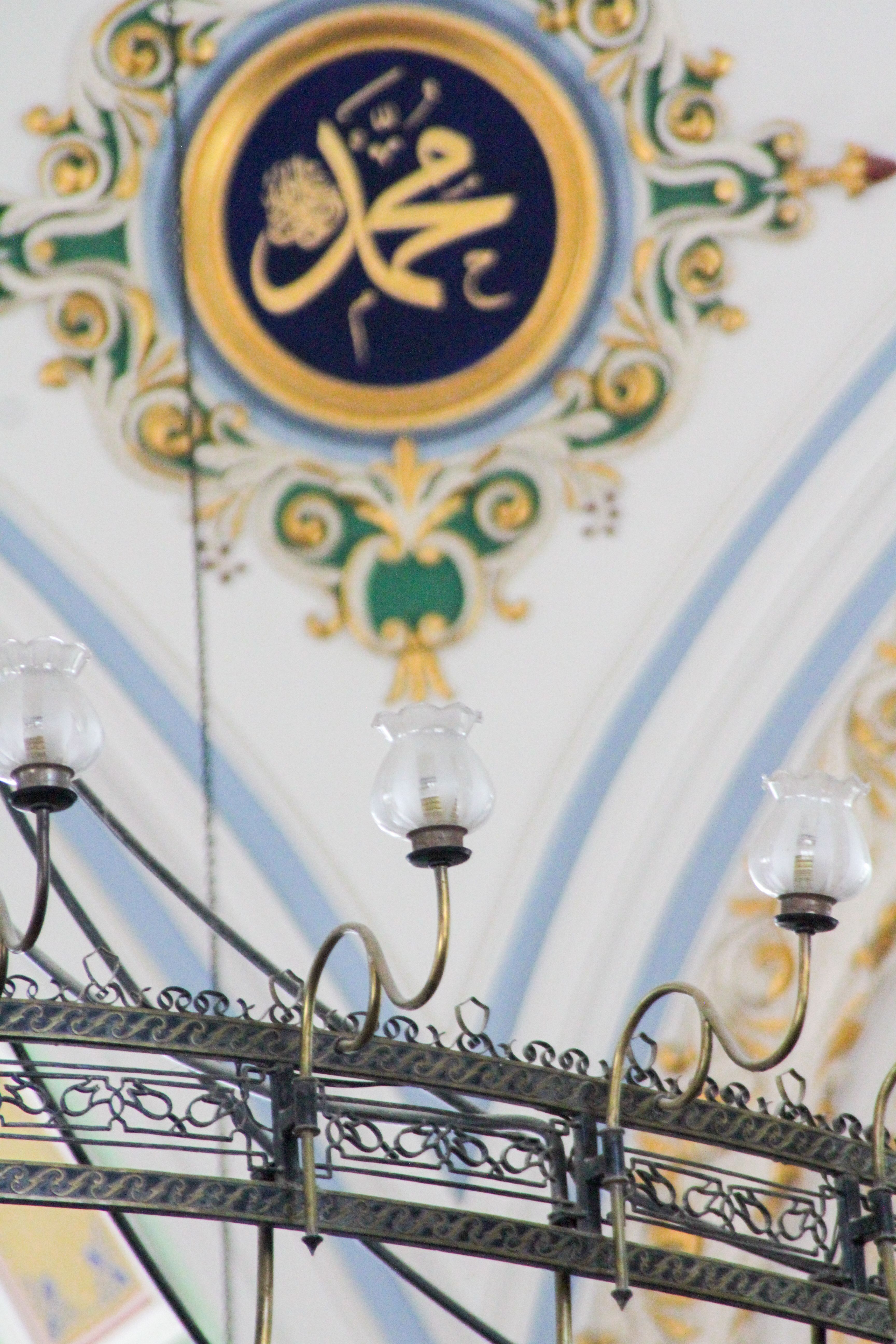 Beautifully decorated mosque ceiling featuring Arabic calligraphy and chandelier detail.