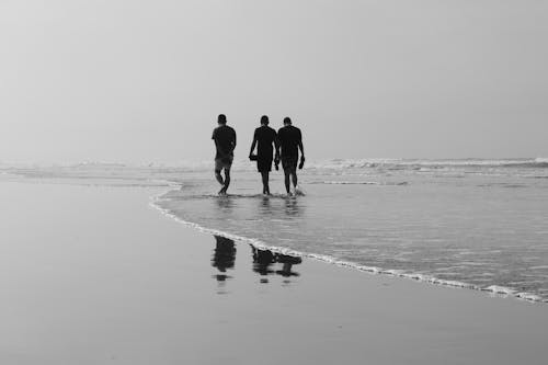 Grayscale Photo of Three People Walking on the Sea Shore