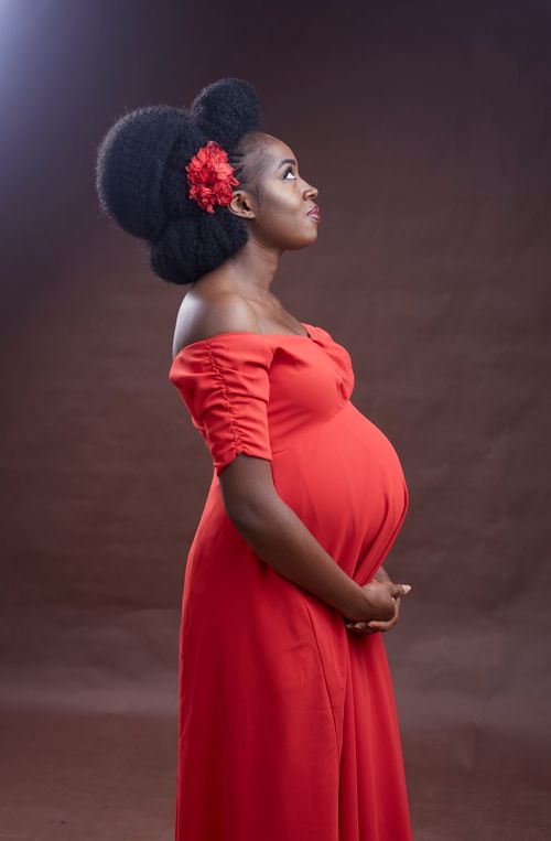 Free A beautiful portrait of a pregnant woman in a red dress exuding elegance and joy. Stock Photo