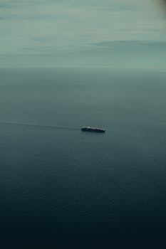 A lone cargo ship navigates the vast ocean, with a serene sky above.