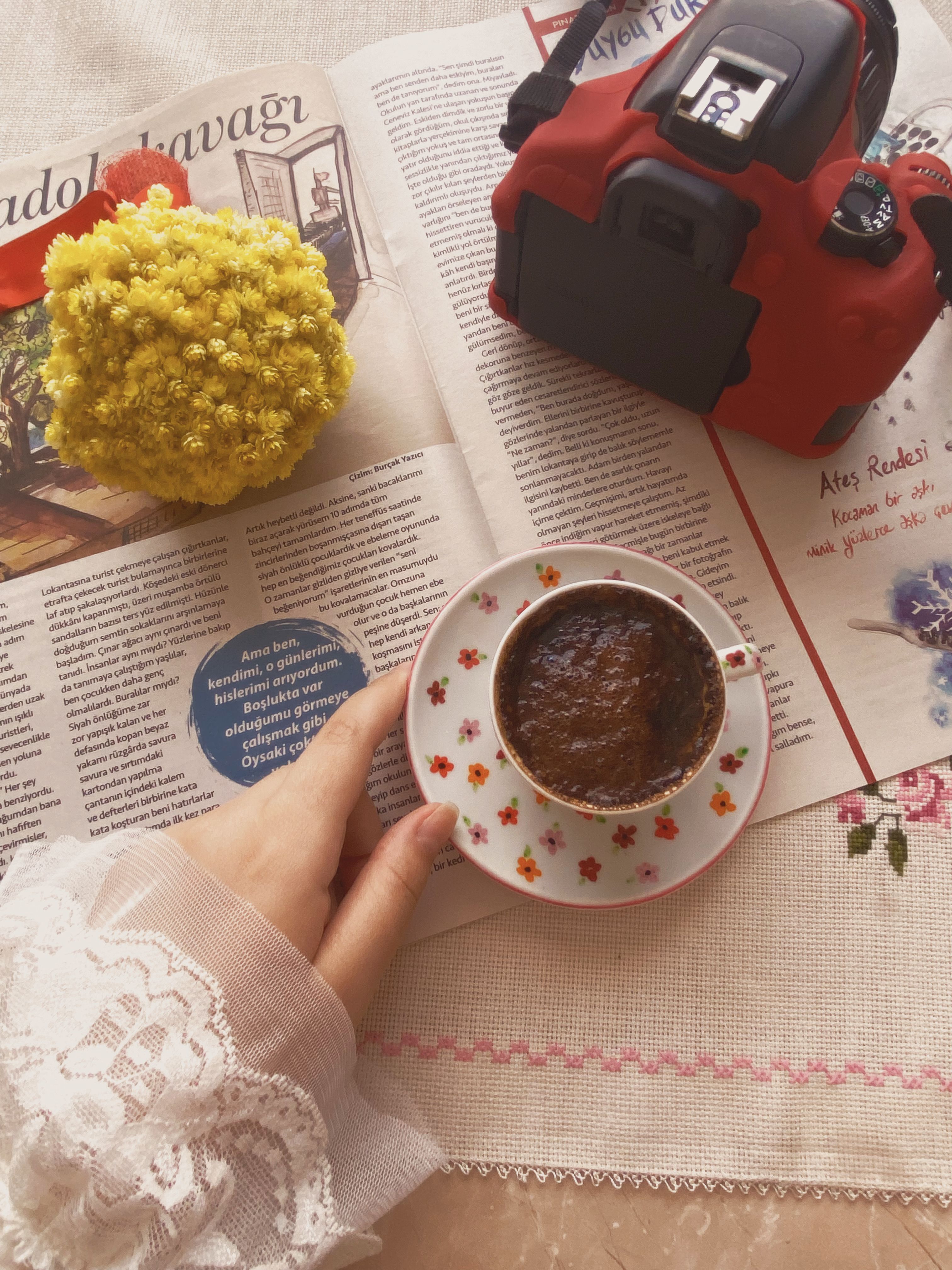 Warm scene with coffee cup, camera, and yellow flowers on a magazine.