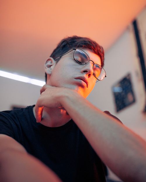 Free A relaxed portrait of a young man in glasses with eyes closed, highlighting a serene moment. Stock Photo