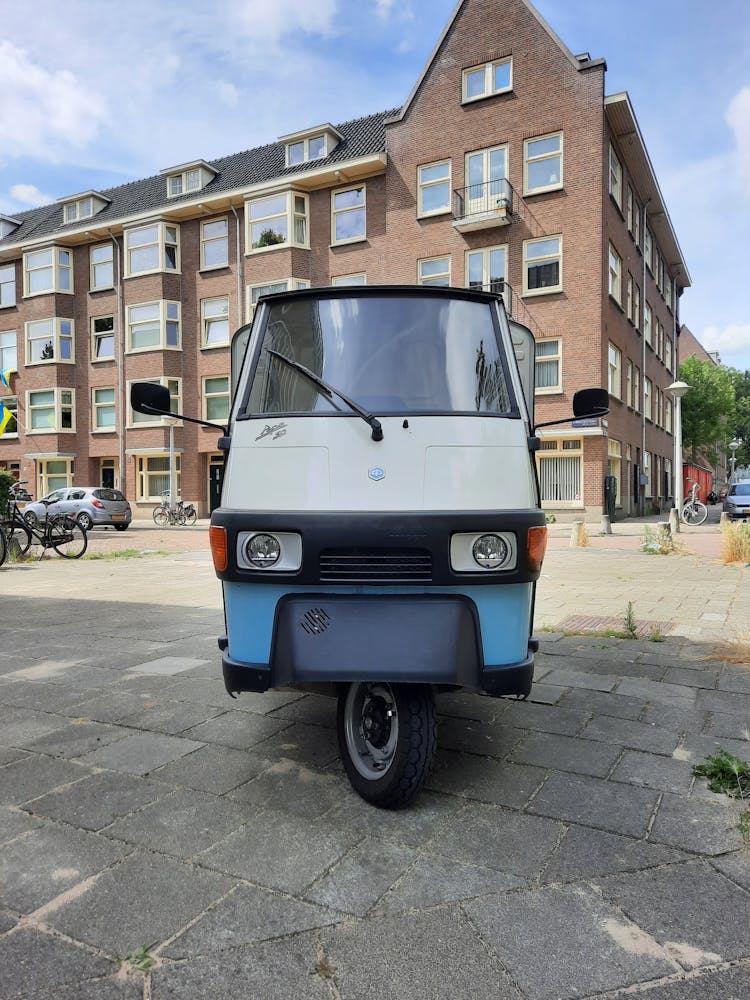 Blue And White Piaggio Ape Car Parked Near The Brick Building 