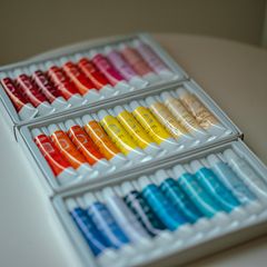 Rows of paint tubes in rainbow order in a white box