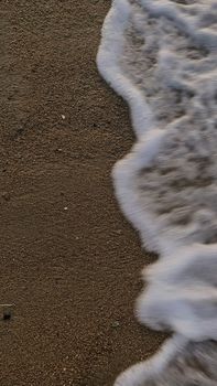 Close-up of ocean waves gently washing over sandy beach creating a tranquil sea foam texture.