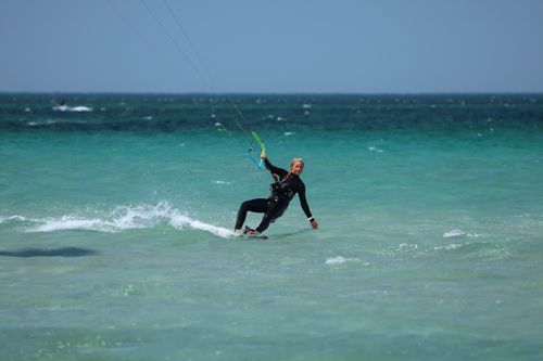 Free Dynamic action shot of a woman kitesurfing on clear turquoise ocean waves under a bright sky. Stock Photo