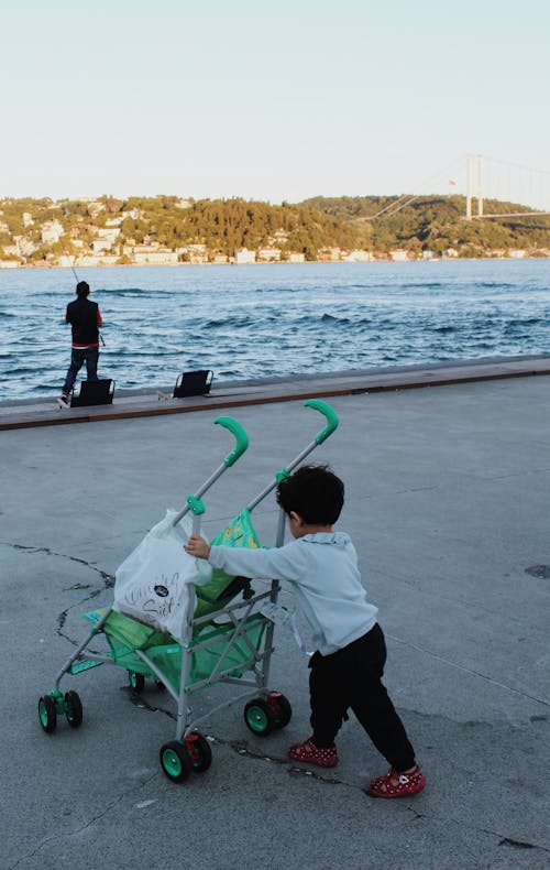 A Little Boy Pushing a Green Stroller on Road