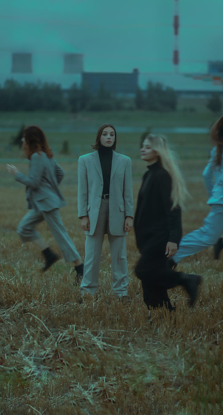 One Woman In A Suit Standing Still And Other Women Running Around Her On A Field 