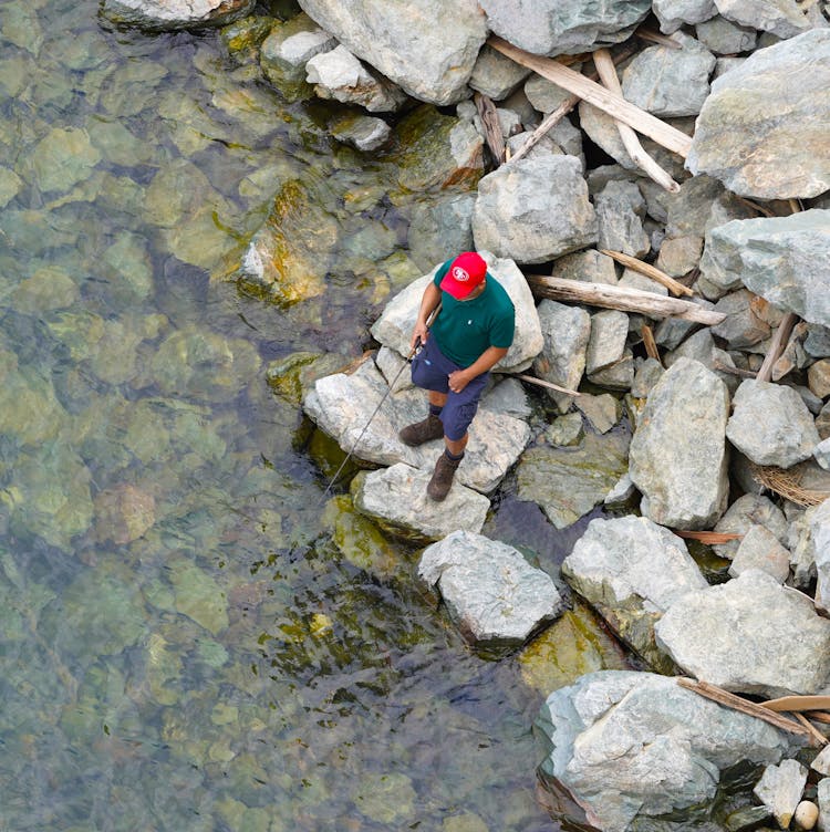 A Man Fishing On Sea While Standing On Rocks