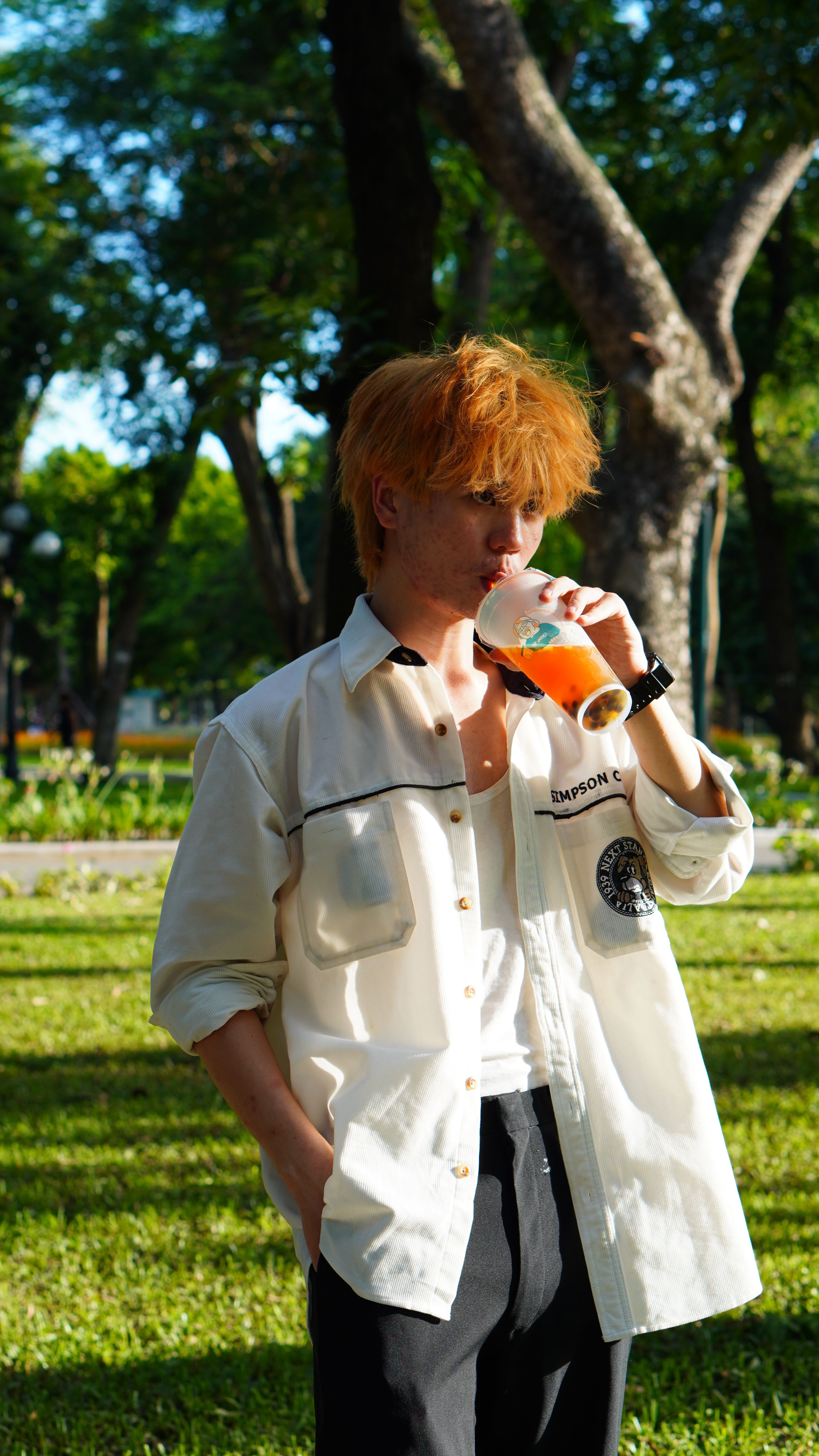Casual young adult sipping a beverage outdoors in a sunlit Hà Nội park.