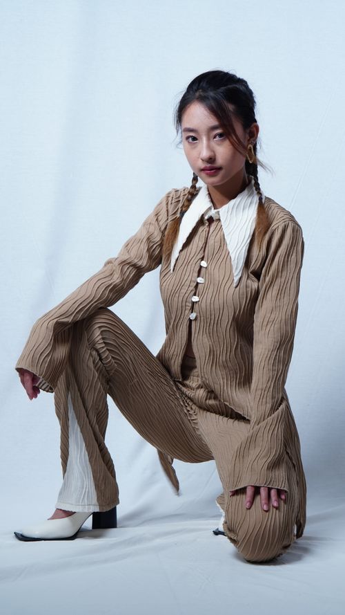 Free Asian woman in fashionable outfit kneeling indoors during a studio shoot. Stock Photo