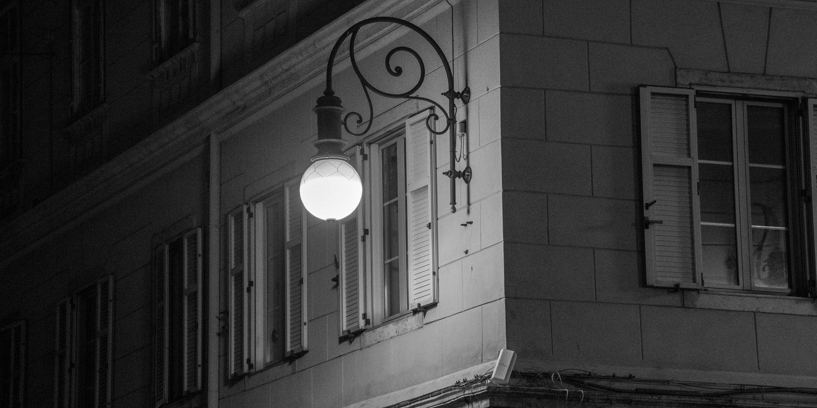 Black and white image of an illuminated streetlight on a historic building corner at night.