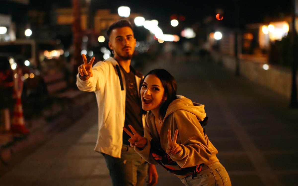 Cheerful friends posing with peace signs on a lively street at night in Năvodari.