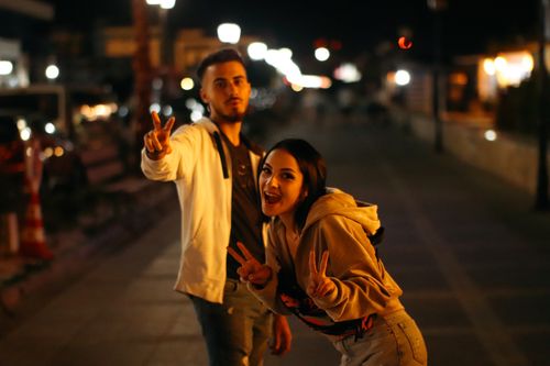 Free Cheerful friends posing with peace signs on a lively street at night in Năvodari. Stock Photo