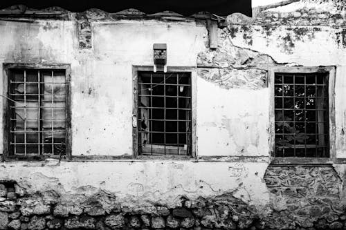Grayscale Photo of an Abandoned House with Decayed Wall and Windows