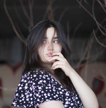 A contemplative woman in a floral dress poses with her hand on her face, capturing a thoughtful mood.
