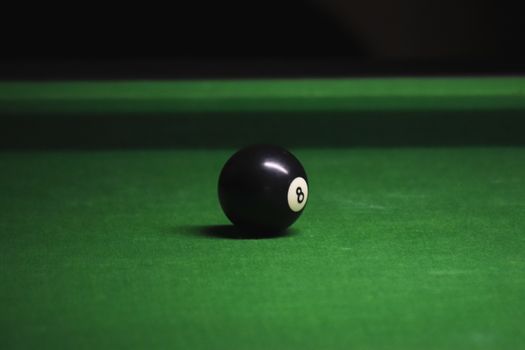 Close-up of black eight ball on a green billiard table with soft lighting.